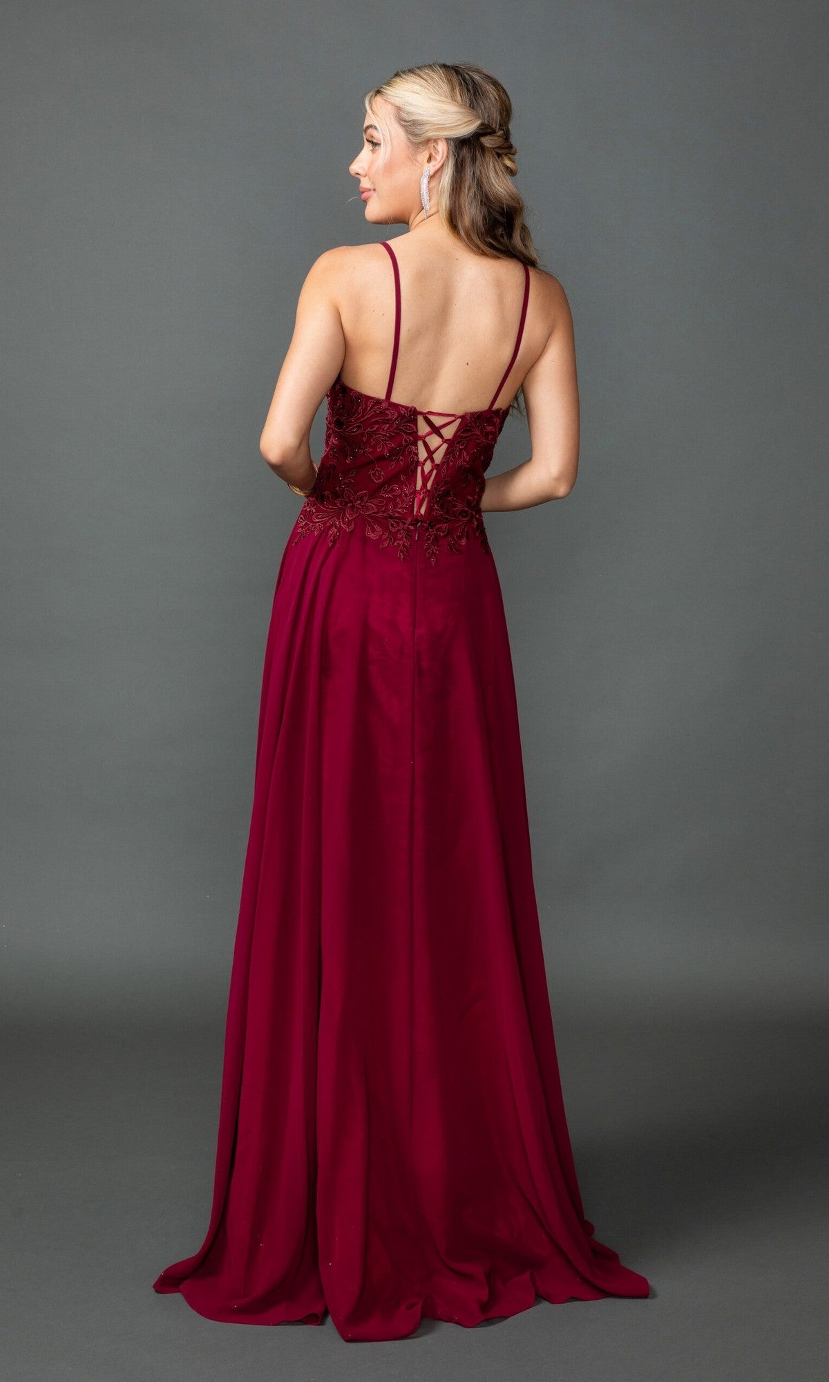 A woman models the Dancing Queen 4542 long prom dress in burgundy, featuring a lace-up back, as she stands facing away against a plain gray background.